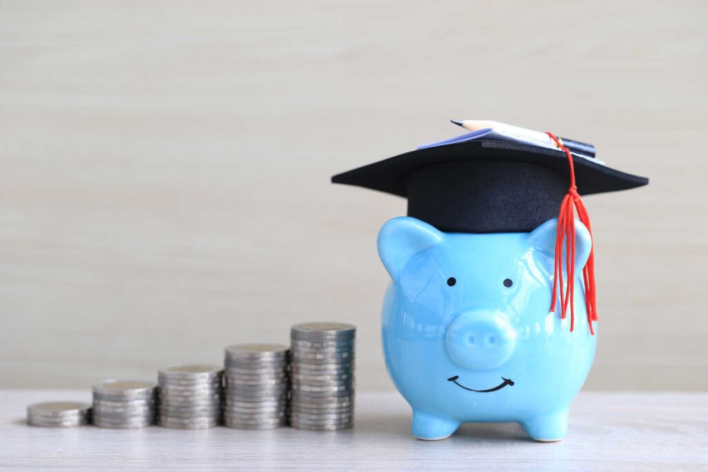 blue piggy bank with graduation cap and quarters stacked to pigs right